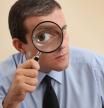 Businessman looking through magnifying glass. Focus on his hand and magnifying glass.