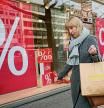 A woman walks with purchases past a store in Berlin, DEU, Friday, April 1, 2022. Inflation in Europe soared to another record, according to new EU figures released Friday, in a fresh sign that rising energy prices fueled by Russia's war in Ukraine are squeezing consumers and adding pressure on the central bank to raise interest rates. (AP Photo/Pavel Golovkin)