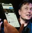 In this photo illustration, a phone screen displays the Twitter account of Elon Musk with a photo of him shown in the background, on April 14, 2022, in Washington, DC. - Tesla chief Elon Musk has launched a hostile takeover bid for Twitter, insisting it was a 