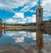 People stand in front of the ruins of the church of Sant Roma de Sau, at the swamp of Sau, located in the province of Girona in Catalonia on August 23, 2022. - The swamp of Sau is a reservoir on the Ter river, created by a dam located in the municipality of Vilanova de Sau. The marsh, built from 1947 to 1962, covered the village of Sant Roma de Sau which is still visible, including the bell tower of the 11th century Romanesque church, when the reservoir water level is low. The church of the Sau swamp is registered as the world's oldest that is preserved upright in water. (Photo by Josep LAGO / AFP)