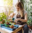 Pretty woman grows tropical plants in her garden. Gardener in working outfit looking after different exotic flower and herb. Close up of woman's hand spraying water on houseplants.