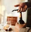 Una persona abriendo una botella de vino con un sacacorchos.