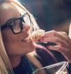 Close up of a happy woman with glasses biting a sandwich.