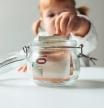 Una niña guardando billetes de euro en un pote de cristal