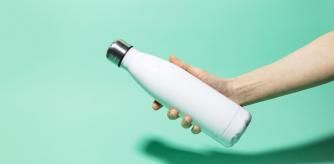 Close-up of female hand holding white reusable steel stainless thermo water bottle isolated on background of aqua menthe color. Plastic free.