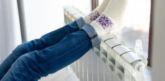 Una mujer se calienta los pies en el radiador frente a una ventana