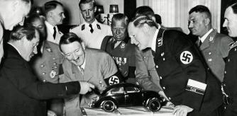 Nazi leader Adolf Hitler (1889 - 1945) admires a model of the Volkswagen car and is amused to find the engine in the boot. He is with the designer Ferdinand Porsche (left), and to the right are Korpsfuhrer Huehnlein, Dr Ley, Schmeer, and Werlin. (Photo by Heinrich Hoffmann/Hulton Archive/Getty Images)