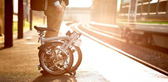 Una persona esperando en un andén de estación con su bicicleta plegable.