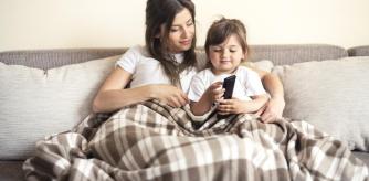 Una madre y su hija en el sofá con una manta viendo la televisión