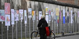 A cyclists looks at placards lined up as an open-air installation marking the former course of the wall in front of wall segments ahead of celebrations marking the 35th anniversary of the fall of the Berlin Wall in Berlin, on November 8, 2024. (Photo by John MACDOUGALL / AFP)