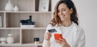 Una mujer mirando el móvil con tarjeta en mano