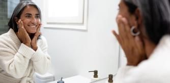 Una mujer se mira el rostro en el espejo contenta