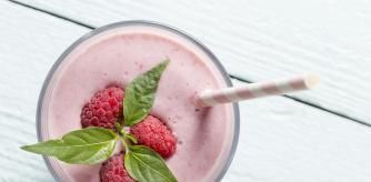 Top view of a raspberry smoothie glass set on a wooden boards, decorated with drinking straw, three raspberries and mint leaves