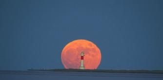 La luna de fresa se deja ver tras el Faro del Fangar.