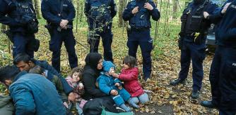 An Iraqi migrant woman with children sits on the ground as they are surrounded by border guards and police officers after they crossed the Belarusian-Polish border during the ongoing migrant crisis, in Hajnowka, Poland October 14, 2021. REUTERS/Kacper Pempel