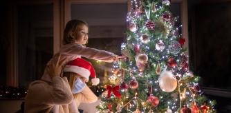Madre llevando a su hija en los hombros decorando el árbol navideño