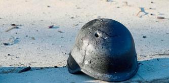 A soldier's helmet with a bullet hole near debris of burning military trucks, in a street in Kyiv, Ukraine, Saturday, Feb. 26, 2022. Russian troops stormed toward Ukraine's capital Saturday, and street fighting broke out as city officials urged residents to take shelter. (AP Photo/Efrem Lukatsky)