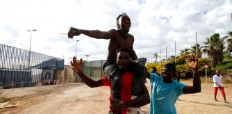 Un grupo de migrantes yacen tendidos en el suelo bajo la vigilancia de la Policía marroquí