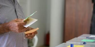 Un hombre sostiene sus papeletas de votación ante las urnas de la mesa en un colegio electoral este domingo.