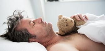 Man sleeping with his bear on his chest, hand on paw.