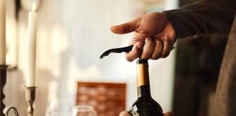 Una persona abriendo una botella de vino con un sacacorchos.