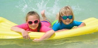 Dos niños bañándose con trajes de baño que les protegen del sol