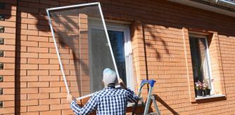 Un hombre instala pacientemente una mosquitera en la ventana