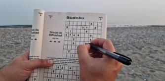 Una persona completa un sudoku mientras pasa un tranquilo día de playa