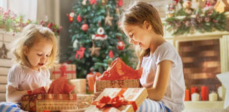 Niños abriendo regalos de Navidad junto al árbol, en un ambiente familiar y festivo.