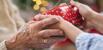 Manos de una persona mayor recibiendo un regalo de Navidad envuelto en papel rojo.