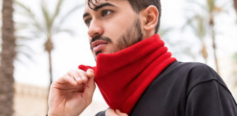 Hombre ajustando una braga de cuello roja al aire libre en un entorno urbano