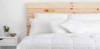 Cama vestida con edredón nórdico blanco y almohadas a juego sobre cabecero de madera clara