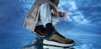 Modelo masculino con zapatillas Geox deportivas en tonos verdes y negros sobre fondo azul reflejado