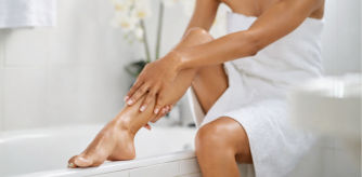 Mujer sentada tocándose la pierna suave recién depilada en un baño luminoso