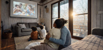 Familia sentada en el salón de una casa viendo una película proyectada en la pared, con luz natural entrando por grandes ventanales