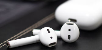 Auriculares inalámbricos tipo AirPods en color blanco junto a su estuche de carga sobre una superficie oscura