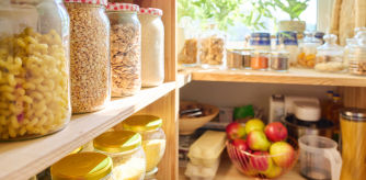 Despensa organizada con alimentos básicos como pasta, legumbres, cereales y frutas en frascos de vidrio