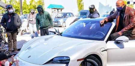 Dwayne Johnson, conocido como la Roca, intenta subir a un Porsche Taycan durante la grabación de una escena de la película Red Notice