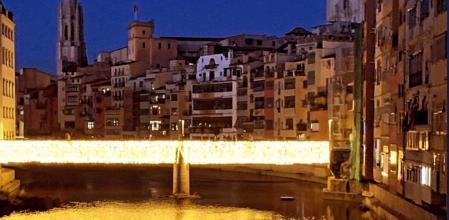 El puente brilla en Girona con la iluminación navideña y los reflejos en el río.