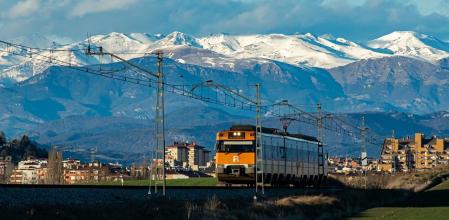 El tren de Vic avanza con los Pirineos nevados de telón de fondo.