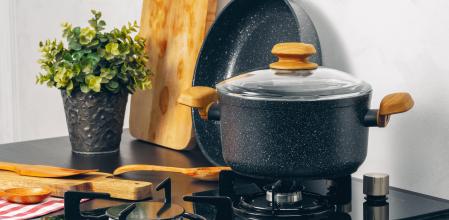 high angle shot of a young caucasian man stirring a lentil stew, with a wooden spoon, in a stainless steel cooking pan placed on a gray rustic wooden table