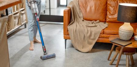 Happy woman with cordless vacuum easy cleaning floor at home in stylish interior design of living room. Smart home concept.