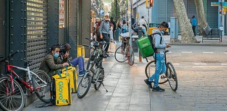 Un grupo de riders de Glovo y Uber Eats esperando pedidos en un restaurante de comida rápida de la calle Ferràn con Las Ramblas