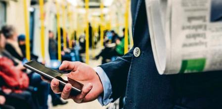 Un hombre con un diario bajo el brazo consulta el teléfono móvil en el metro.