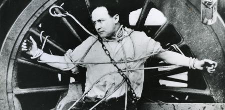 In a publicity stunt, magician and escape artist Harry Houdini (1874 - 1926) chains himself to a locomotive wheel for an escape attempt, ca.1910. (Photo by Transcendental Graphics/Getty Images)