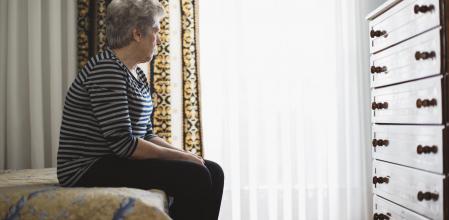 señora de avanzada edad sola mira sentada en el borde de la cama