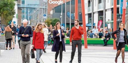 People take a lunch break in the business and financial sector of Dublin City centre with the Google offices in the background on October 7, 2021. - The government of Ireland, one of the few countries to have resisted a global minimum tax on multinational firms, will meet on Thursday to decide whether to join the international reform. Cabinet ministers are due to meet in Dublin in the late afternoon with a decision on accepting the 15 percent rate set to be announced in the early evening, a government spokesman told AFP. (Photo by PAUL FAITH / AFP)
