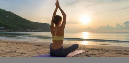 Woman practices yoga. Adult woman raising hands while meditating against colorful morning sky
