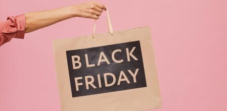 Una mano sujeta una bolsa de compra de Black Friday en un fondo de color rosa