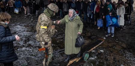 Un militar ucraniano ayuda a una mujer a cruzar el puente de Irpín, cerca de Kyiv